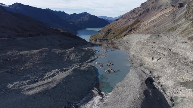Aerial flyover along the glacial tongue of Glacier de Cheilon on a sunny summer day in the Swiss Alps with a pan down view towards the icy blue glacial lake.