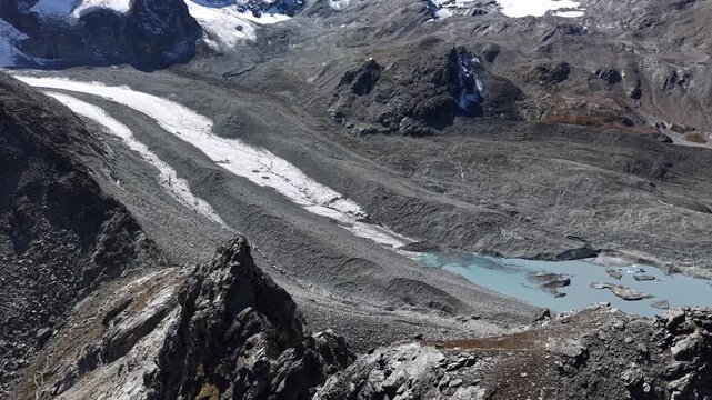 Aerial flyover over the cliifs next to Glacier de Cheilon near Arolla, Switzerland with a pan up view from the glacial lake up to the sunlit mountain peaks like Mont Blanc de Cheilon in the distance