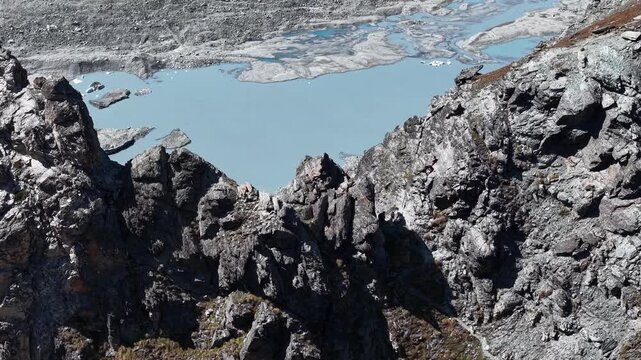 Aerial flyover above the mountain peaks next to Glacier de Cheilon near Arolla, Switzerland with a view of the iceberg filled glacial lake in the distance