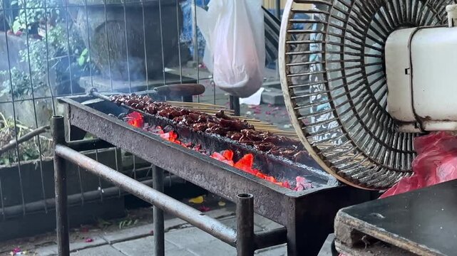 raditional charcoal grill for satay with glowing red embers and smoke, street food preparation concept