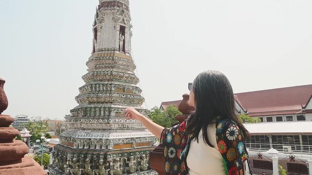 Bangkok, Thailand - 15th february, 2024: Bangkok Wat Arun Temple of Dawn, woman tourist point toward ornate prang tower, Thai Buddhist architecture with ceramic mosaic details, travel sightseeing