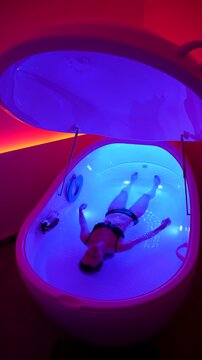 Woman floating in hyper-saline sensory deprivation pod under ambient light, wellness and mental health, relaxation therapy and stress relief.