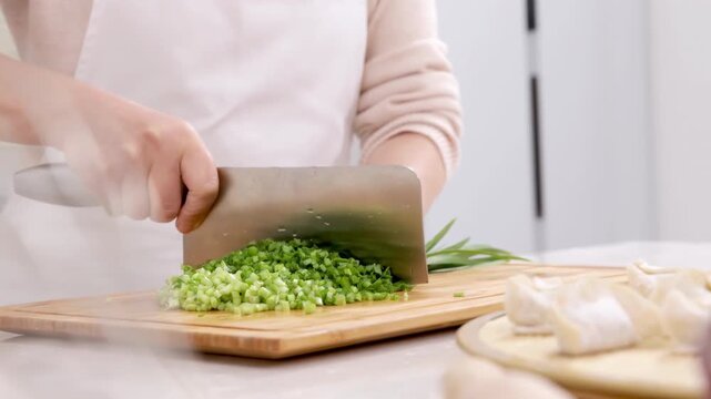 Unidentified hands woman baker chef chopping fresh chives or cutting green onions on a kitchen cutting board with knife to making tasty homemade dumplings stuffed with minced meat and vegetable