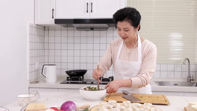 Portrait of elderly woman baker chef wear apron making tasty homemade dumplings stuffed, process of stirring minced meat and vegetable in bowl on home kitchen table