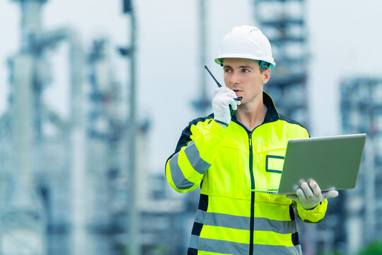 Male petroleum refinery engineers and industrial worker working on laptop computer, inspection oil refinery plant at construction site at night, technician maintaining energy power gas system