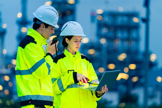 Petroleum refinery engineers and industrial workers working on laptop computer, inspection oil refinery plant at construction site at night, technician teamwork maintaining energy power system