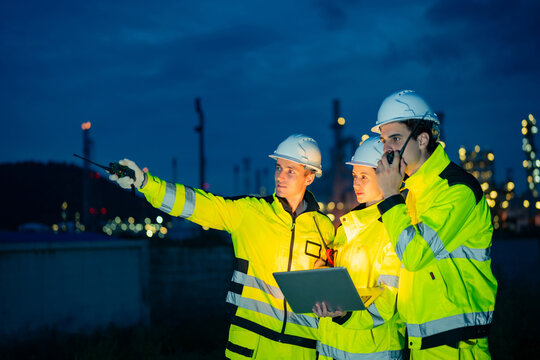 Petroleum refinery engineers and industrial workers working on laptop computer, inspection oil refinery plant at construction site at night, technician teamwork maintaining energy power system
