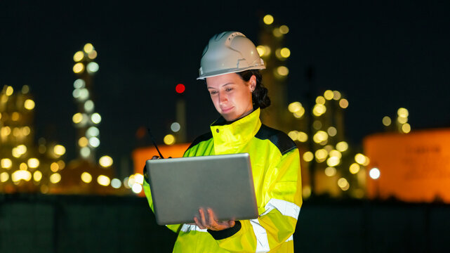 Female petroleum refinery engineers and industrial worker working on laptop computer, inspection oil refinery plant at construction site at night, technician maintaining energy power gas system