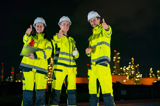 Petroleum refinery engineers and industrial workers working on laptop computer, inspection oil refinery plant at construction site at night, technician teamwork maintaining energy power system