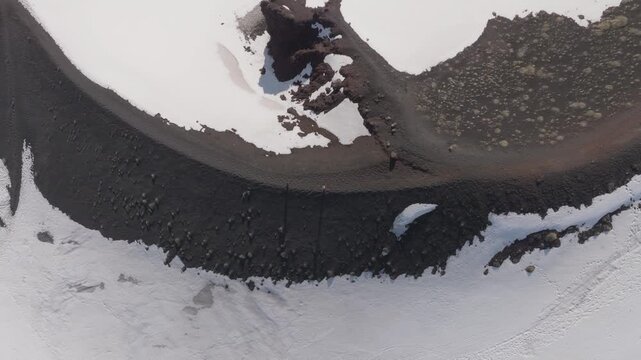 Aerial view of the volcanic crater rim near Rifugio Sapienza with dark volcanic soil and patches of snow in Nicolosi, Sicilia, Italy.