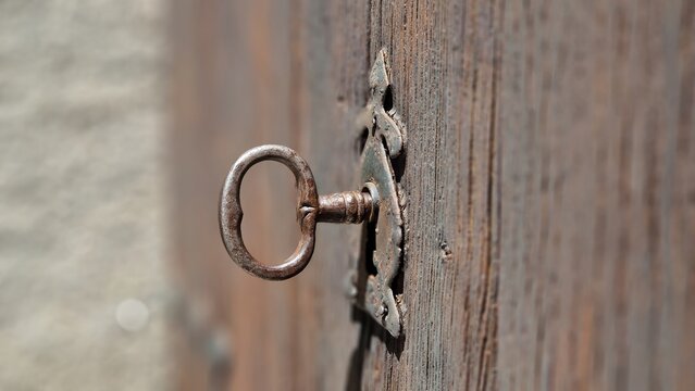 Old rusty key inserted into vintage keyhole on weathered wooden door