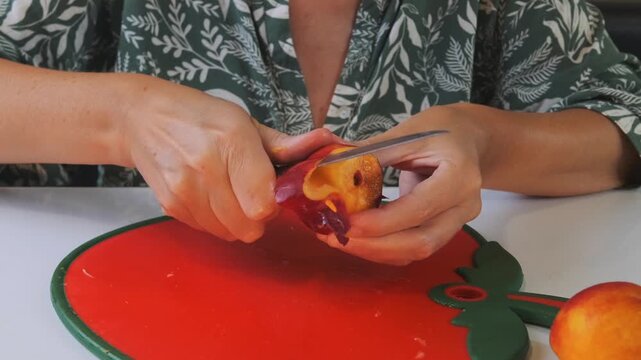 Woman slicing and peeling ripe nectarine on cutting board, front view of hands cutting fresh fruit, food preparation process for dessert or healthy snack, home kitchen cooking