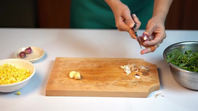 Woman peeling shallots on wooden cutting board with corn and spinach