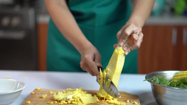 Woman hands slicing fresh sweet corn kernels on a wooden board for cooking
