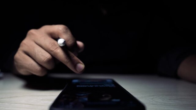 Hand using stylus on tablet touchscreen in low light, Close-up of a person using a stylus and finger on a tablet screen on a wooden desk in low light