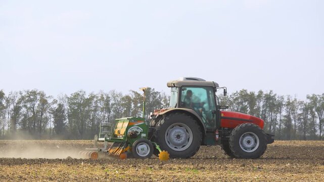 Side view of agricultural tractor with seed drill plowing field during corn sowing, modern farming machinery cultivating soil and preparing farmland for crop planting in rural countryside