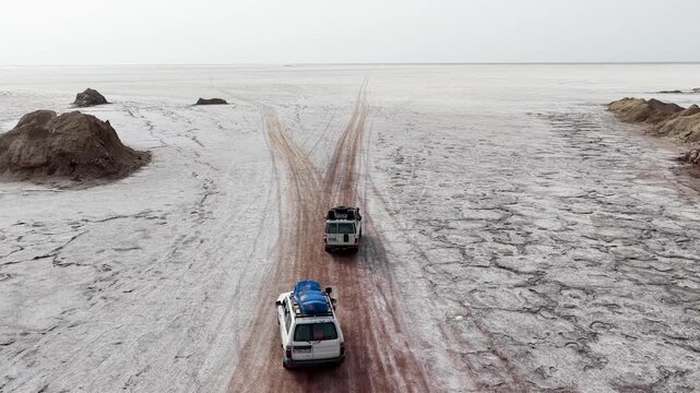 Aerial view of two off-road vehicles driving along a dirt track across the vast salt flats of the Danakil Desert Dalol, Afar, Ethiopia.