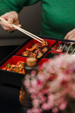 Girl eats food in sauce from bento box with chopsticks. Flash