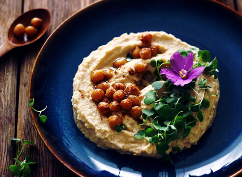 Hummus decorated with microgreens, chickpeas and violet flowers