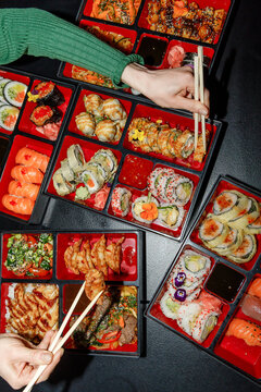 Girl holding sushi roll from bento box with chopsticks. Flash.