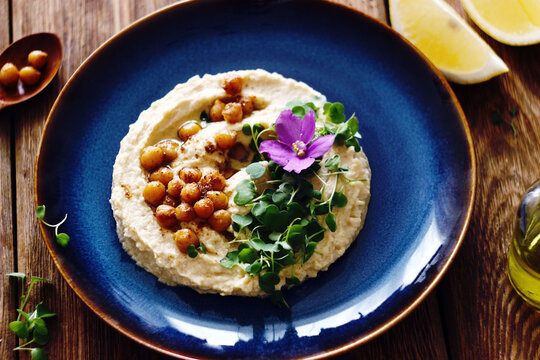 Hummus decorated with microgreens, chickpeas and violet flowers