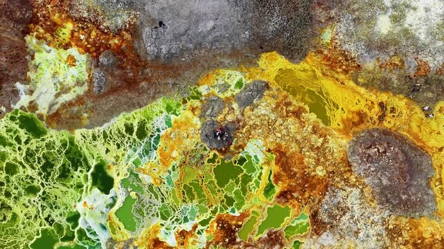 Aerial view of Danakil Desert hydrothermal pools with vibrant yellow mineral deposits and people standing on a central rock in Dalol, Afar, Ethiopia.