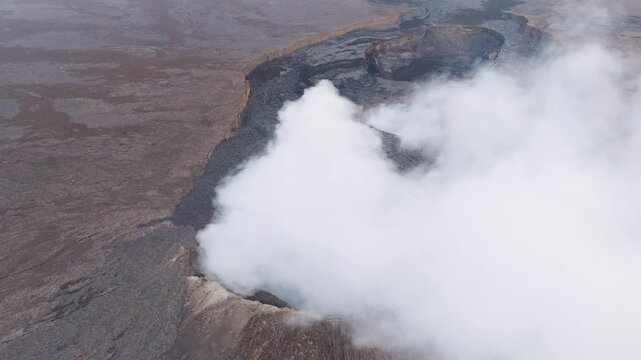 Aerial view of Erta Ale Volcano with thick white smoke rising from the crater over the dark volcanic landscape in Danakil Desert, Afar, Ethiopia.