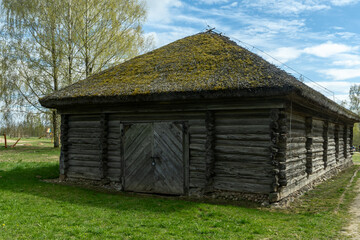 Old log barn with thatched roof in traditional village. Authentic rural heritage building made of timber logs with mossy rooftop at spring landscape © kalyanby