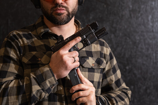 Close-up of a man reloading a modern handgun with a flashlight and red dot sight during tactical training at an indoor shooting range.
