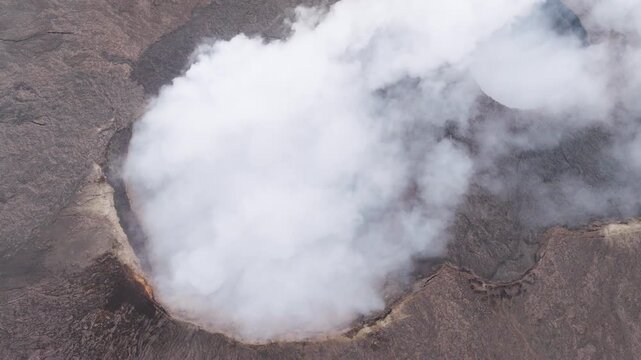 Aerial view of thick white smoke and steam rising from the Erta Ale Volcano crater surrounded by dark volcanic rock in Danakil Desert, Afar, Ethiopia.