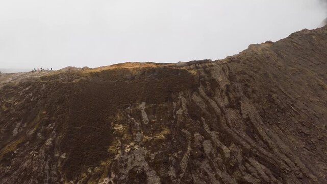 Aerial view of people standing on the rugged rim of Erta Ale Volcano with dark volcanic rock under a hazy sky in Danakil Desert, Afar, Ethiopia.