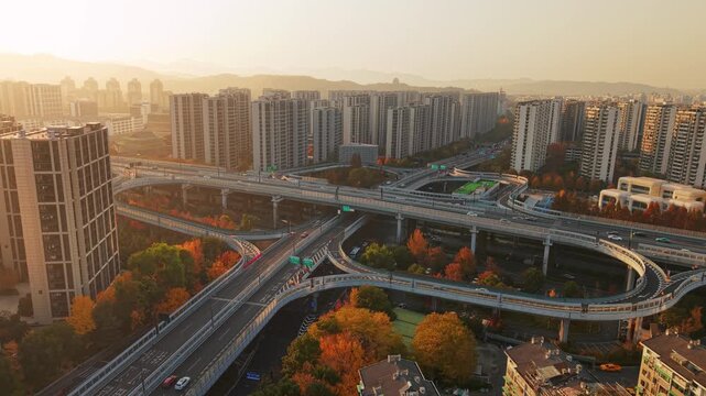 An overhead shot shows cars moving on a highway interchange with colorful autumn trees