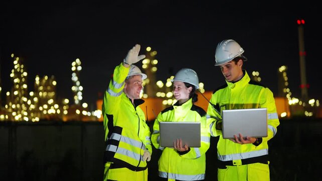 Petroleum refinery engineers and industrial workers working on laptop computer, inspection oil refinery plant at construction site at night, technician teamwork maintaining energy power system