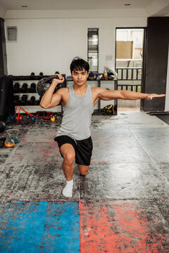 Young man performs a half kneeling kettlebell stability exercise to improve shoulder strength, balance, coordination and core control in gym
