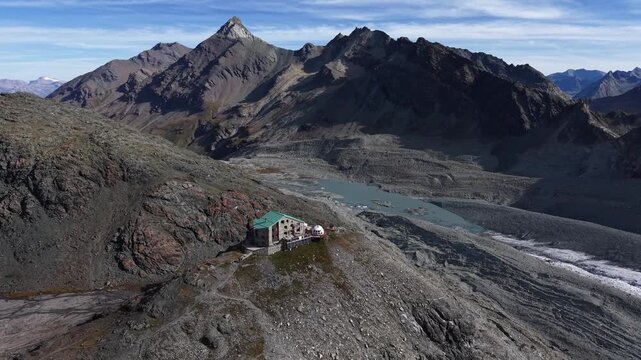 Aerial flyover of a mountain hut alongside Glacier de Cheilon as the morning sun shines over the mountain peaks of Swiss Alps in the Arolla region and Dixence valley