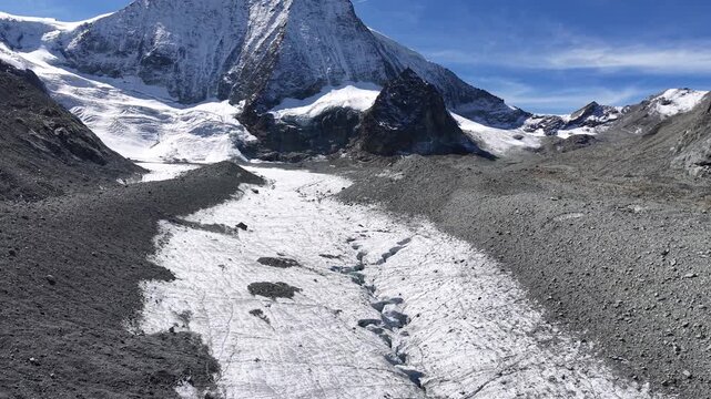 Aerial flyover over the ice of Glacier de Cheilon with the mountain peaks of Swiss Alps in the Arolla region in the background on a sunny summer day