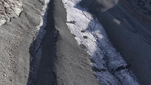 Aerial flyover over the glacial tongue of Glacier de Cheilon on a sunny summer day in the Swiss Alps with a pan up view towards the mountain peaks of Arolla such as Mont Blanc de Cheilon