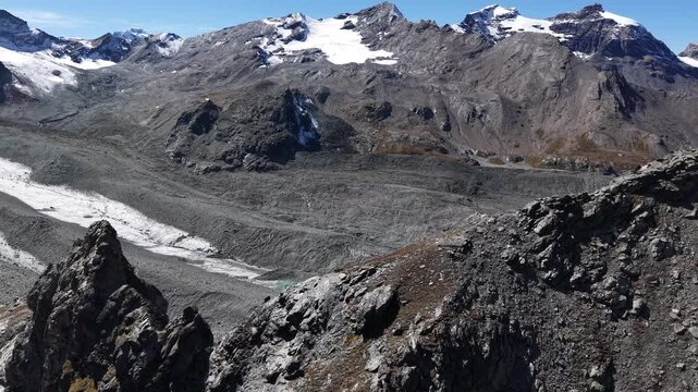 Aerial flyover over the mountain peaks next to Glacier de Cheilon near Arolla, Switzerland with a view of the glacial lake in the distance and a hiking trail leading to the Pas de Chevre ridge