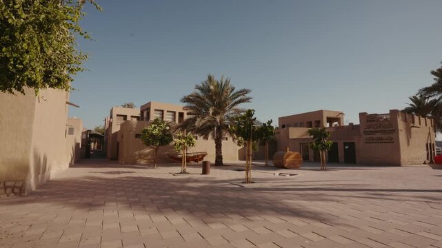 Static shot of empty sandy courtyard with traditional adobe architecture, palm trees, and paved plaza under clear blue sky. &middot; 4K DCI 25fps