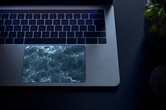 Top view of a laptop trackpad with real ocean waves rippling beneath glass