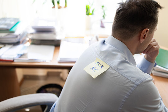 Office prank with kick me message on sticky note. Funny day. April fish. Practical jokes. Inscriptions on the back. Stickers with jokes. Rear view of businessman with sticky note on his back in office