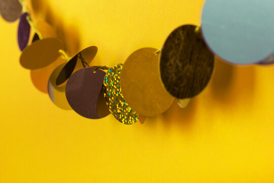 Close-up of colorful metallic disc garland on yellow background.