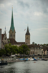 Fototapeta premium View of Fraumünster and St. Peter Church Towers over the Limmat River on a Cloudy Day in Zurich, Switzerland