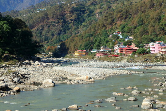 Himalayan river landscape with hillside town in Uttarkashi, Uttarakhand India. Beautiful natural landscape of a Himalayan river flowing through a rocky valley with colorful hillside buildings.