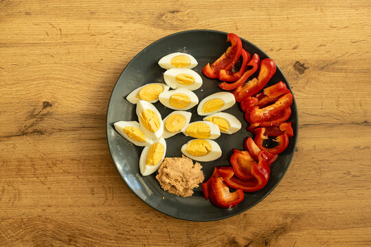 Top view of healthy breakfast. Hard boiled eggs on a plate, salmon pate and red pepper. Wood background