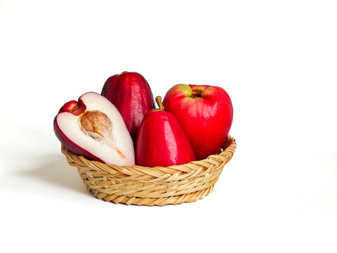 Fresh red to deep red wax apple (Syzygium samarangense) fruit in a small woven bamboo basket, whole and halved pieces showing inner flesh and seed, isolated on white background
