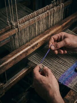 Detailed view of weaver hands working on ancient wooden loom with purple and gray wool threads
