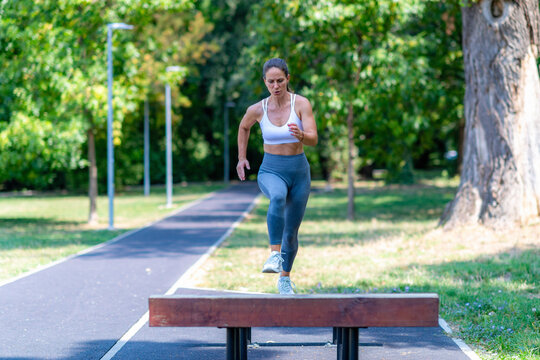 Woman stepping over wooden obstacle in park, performing functional training and agility workout outdoors.