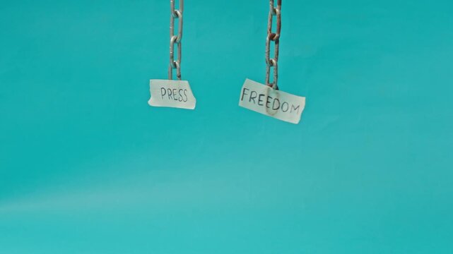 Small Paper Signs For "Press" And "Freedom" Hang From Metal Chains Against Blue Background For Imprisonment Of Independent Media