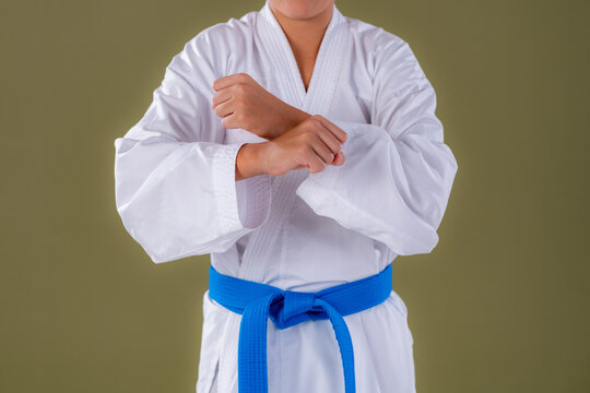 Boy in white karate uniform with blue belt crossing arms in front as part of a preparatory pose. Highlights discipline, focus, and structured martial arts movement.